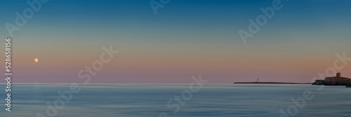 Sunset over Meditteranean sea in Menorca with lighthouse and full moon