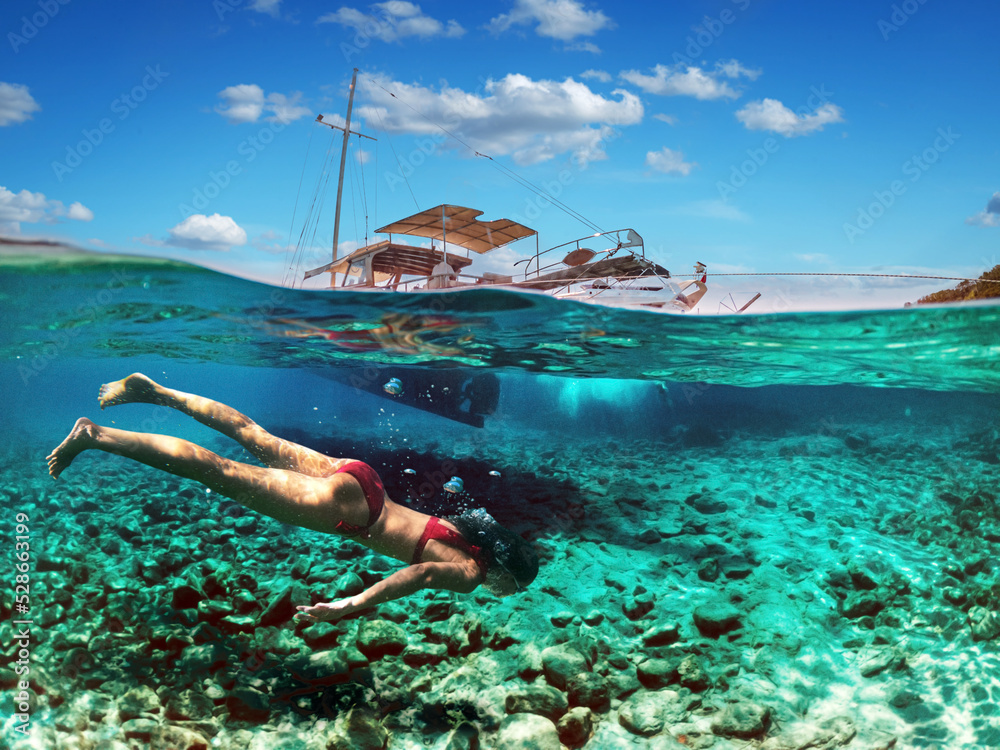 Woman diver is snorkeling on a beautiful sea beach. The bottom half of the picture is occupied by the seabed, on the top - the coast with a yacht and a beautiful sky.