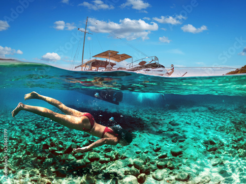 Woman diver is snorkeling on a beautiful sea beach. The bottom half of the picture is occupied by the seabed  on the top - the coast with a yacht and a beautiful sky.