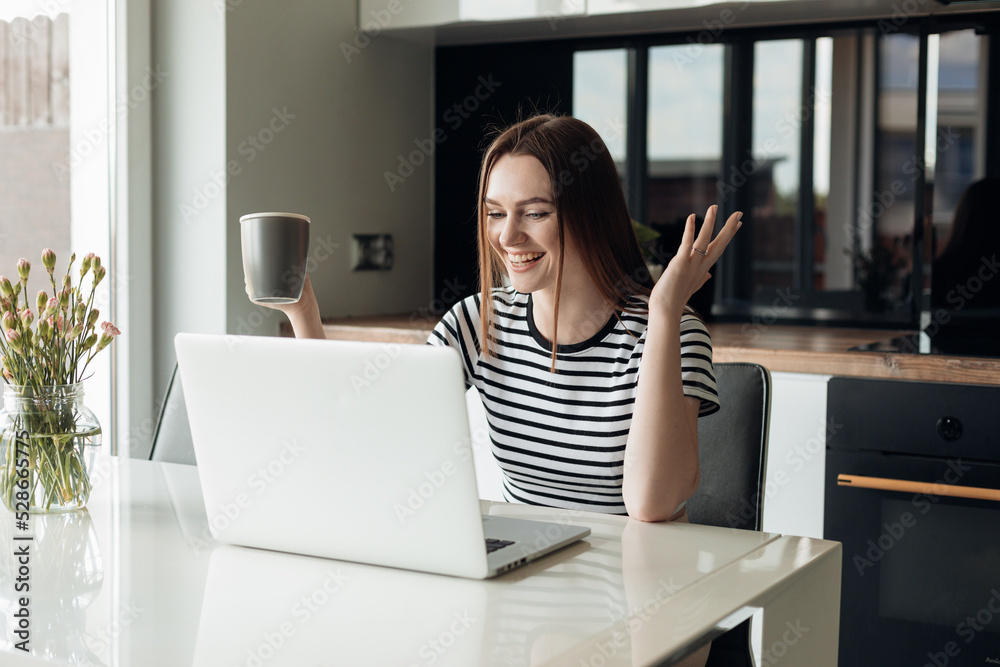 Young laughing and cheerful female using white laptop and drinking coffee. Video call webinar, conference, remote job Young laughing and cheerful female using white laptop and drinking coffee. Video call webinar, conference, remote job