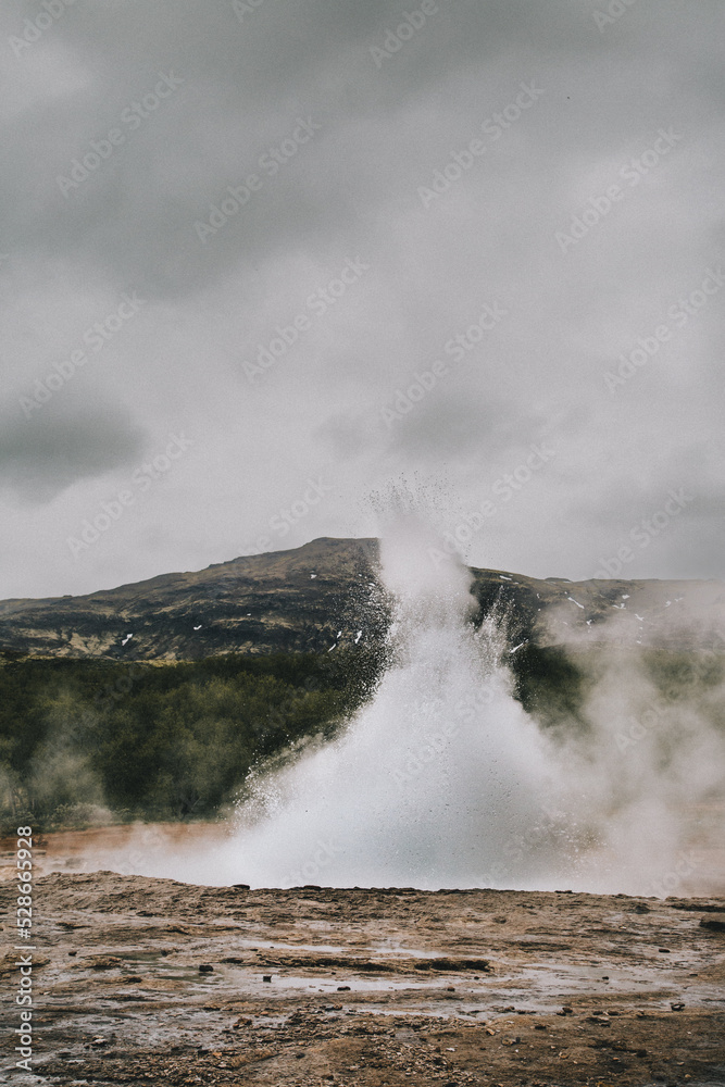 Geysir erupting in front of mountain