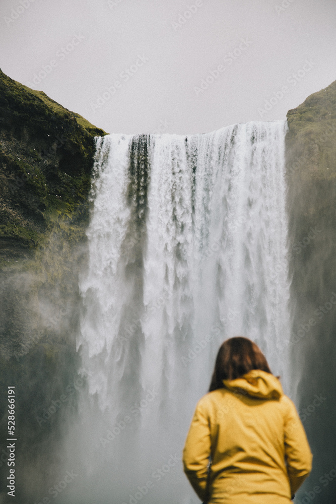 Woman in bright yellow coat standing in front of Skogafoss waterfall