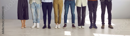 Cropped indoor low section shot of people's legs. Group of employees of different sexes and genders in pants and jeans standing in row on office floor. Banner. Smart and casual work dress code concept