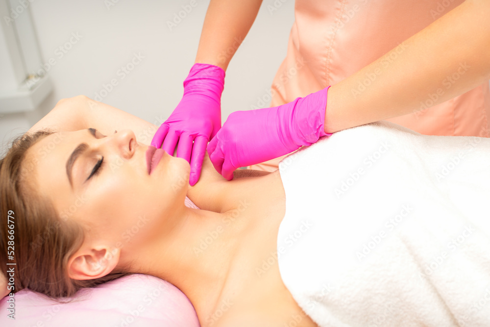 Fototapeta premium Waxing. Depilation under the armpits of the young woman lying with closed eyes in the spa salon
