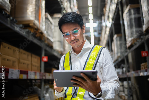 A male worker working in a warehouse uses a digital tablet to inspect the goods on the shelves to manage the products in the warehouse. Logistics business planning concept. Industrial concept.