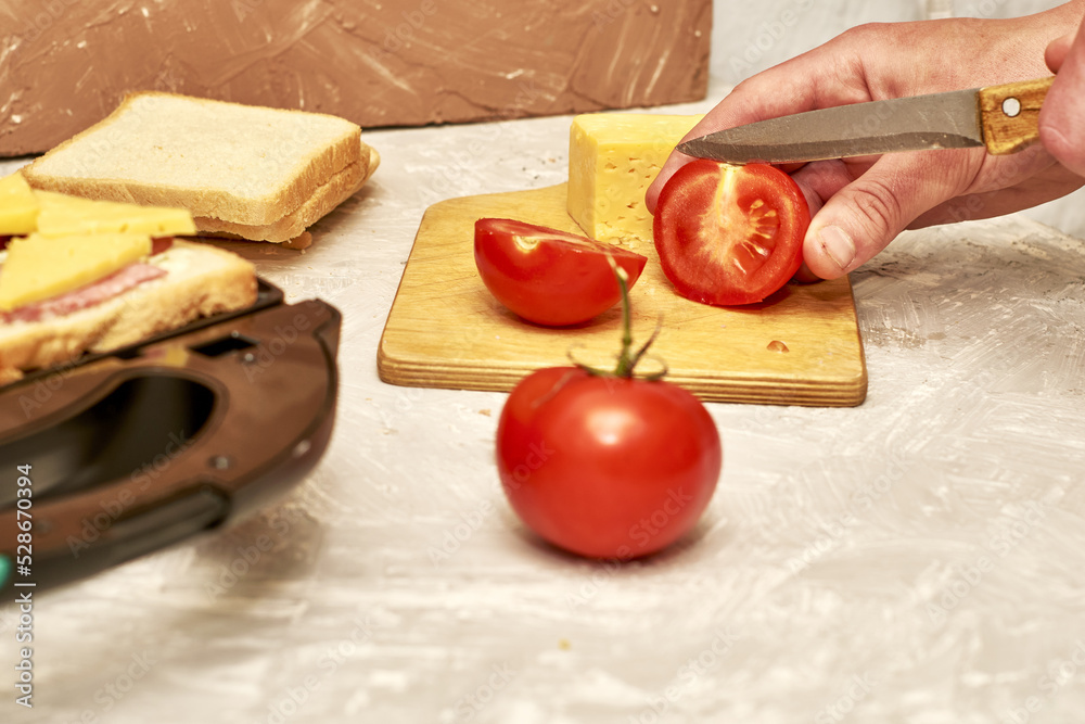 a man making sandwiches in a sandwich maker cuts tomatoes on a cutting board a man making sandwiches in a sandwich maker cuts tomatoes on a cutting board