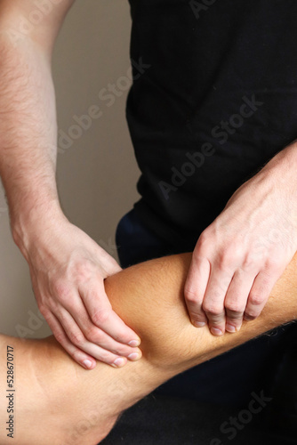 Masseur does legs massage in spa center on gray concrete background. Massage of myofascial trigger points on leg of male client to release tension. Rehabilitation, sport therapy medicine.