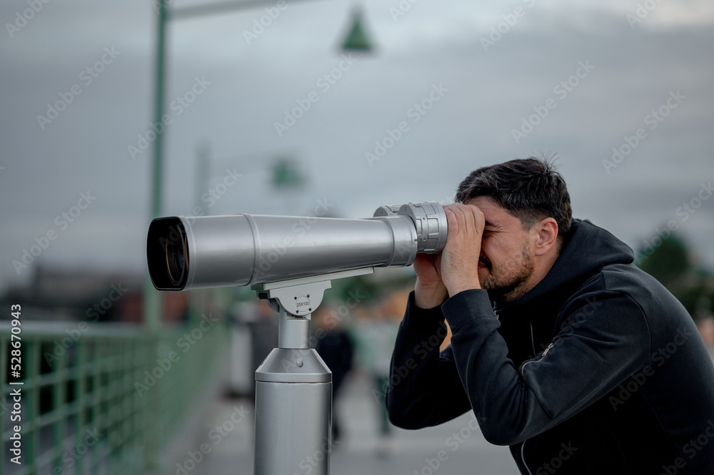 a man in the evening in the city looks at the sights with large binoculars
