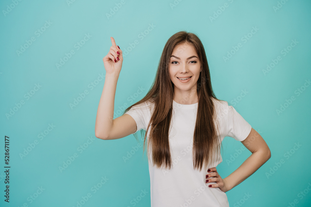 Pretty blonde caucasian young woman in white t-shirt with loose hair points up at empty space by index finger, smiles wide. Cute Italian girl looking at camera, promoting, sale, discount, new offer. Pretty blonde caucasian young woman in white t-shirt with loose hair points up at empty space by index finger, smiles wide. Cute Italian girl looking at camera, promoting, sale, discount, new offer.