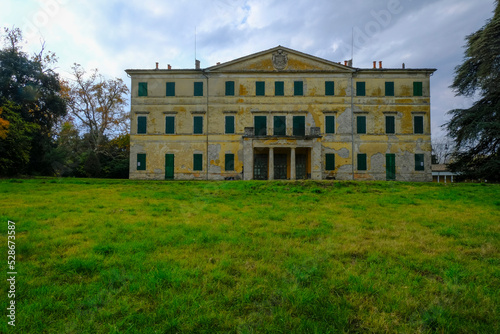 Yellow facade of the Villa Casino dei Boschi across the green meadow and dramatic sky. Boschi di Carrega, Emilia-Romagna, Italy