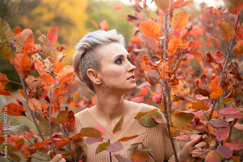 portrait of hipster woman with short hair in autumn park background with red and golden trees