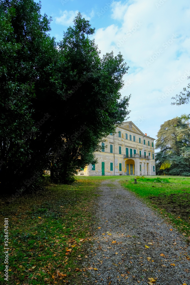 A pathway going to yellow facade of the Villa Casino dei Boschi across the green meadow and dramatic sky. Boschi di Carrega, Emilia-Romagna, Italy