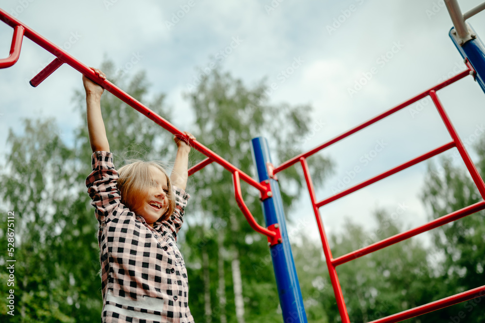 Obraz premium the girl is hanging on a horizontal bar on the playground, the child is engaged in sports
