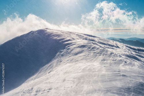 Sunbeams over a mountain range covered with ice and snow. Strong wind on a mountain top covered with snow.