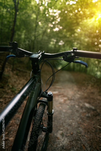 Bicycle frame, air suspension fork and handlebar with brake handle with forest background. Concept of using MTB on a path in the woods. © AlexGo