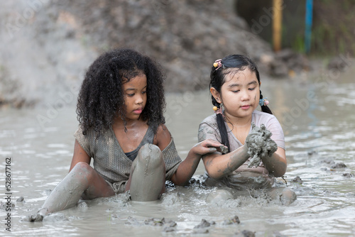 Group of happy children girl playing in wet mud puddle on summer day