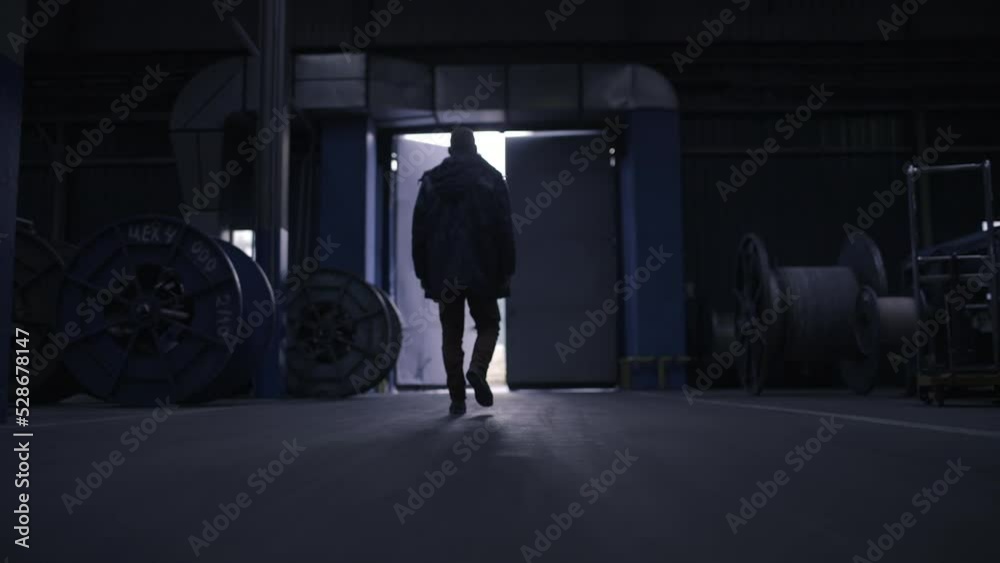 A male production worker goes through the factory to the exit. The camera behind follows him. Dark room, out into the light. A factory worker finishes his shift. 4K