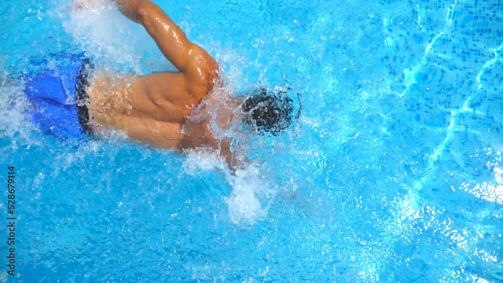 Top view of sporty guy swimming across pool splashing crystal clear water. Unrecognizable man floating and enjoying recreation on resort in summer sunny day. Concept of vacation. Close up Slow motion
