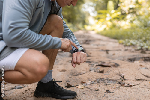 Close up man using smart watch to monitor performance, setting up his smart watch before exercise on path forest.