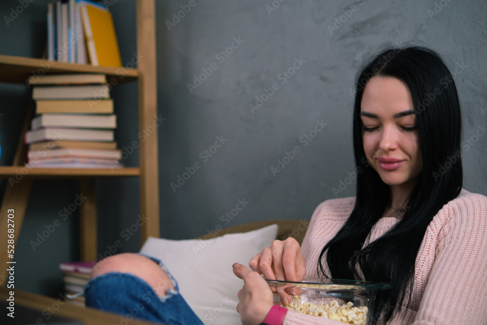 A girl in a pink sweater eats popcorn from a glass bowl while watching a movie on a laptop