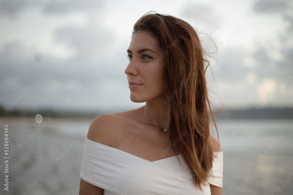 Portrait of young woman at ocean side looking at camera. Smiling female standing at the beach. Portrait of young woman at ocean side looking at camera. Smiling female standing at the beach.