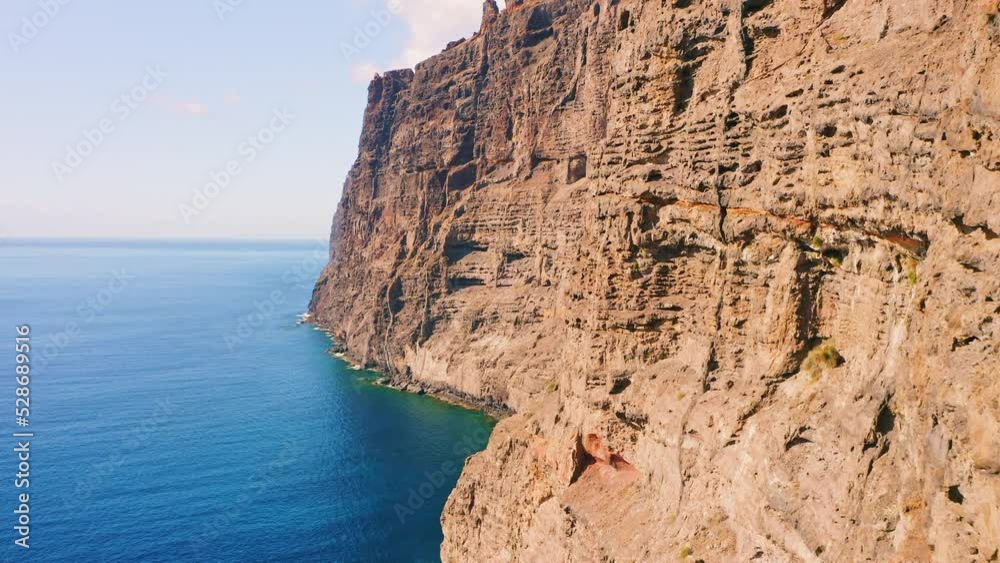 Lifeless mountains. Drone flight over huge rocks. Aerial Los Gigantes cliffs, Tenerife. Atlantic ocean. Camera movement from a rocky coast to the deep blue sea. Cape in the background. Sunny day. Lifeless mountains. Drone flight over huge rocks. Aerial Los Gigantes cliffs, Tenerife. Atlantic ocean. Camera movement from a rocky coast to the deep blue sea. Cape in the background. Sunny day.