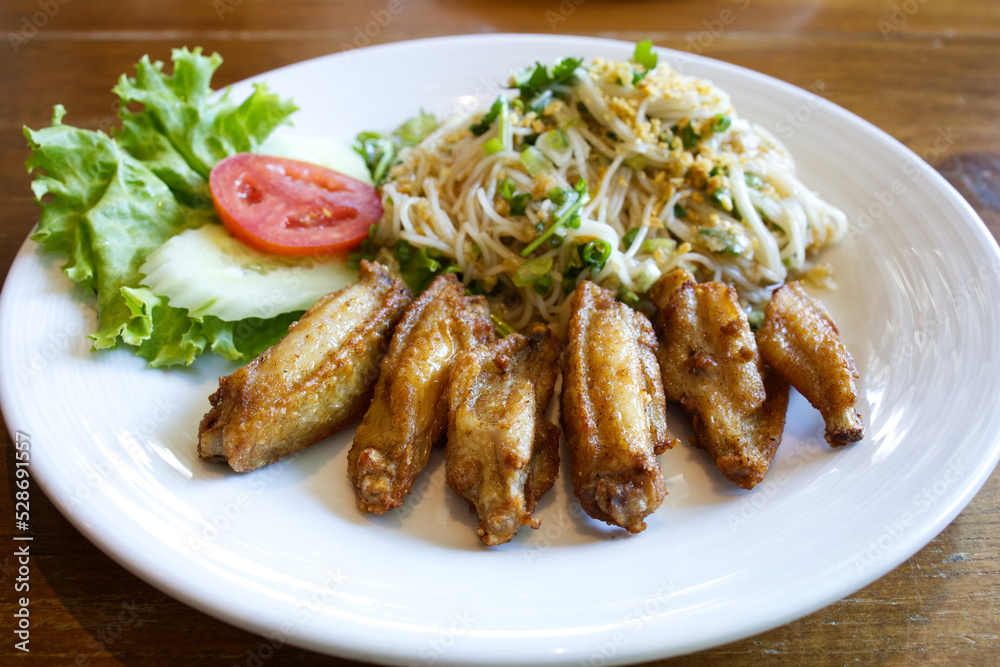 Fried wing chicken served with spicy rice flour noodle salad and vegetables; cucumber, tomato, and green lettuce from Thailand. Fried wing chicken served with spicy rice flour noodle salad and vegetables; cucumber, tomato, and green lettuce from Thailand.