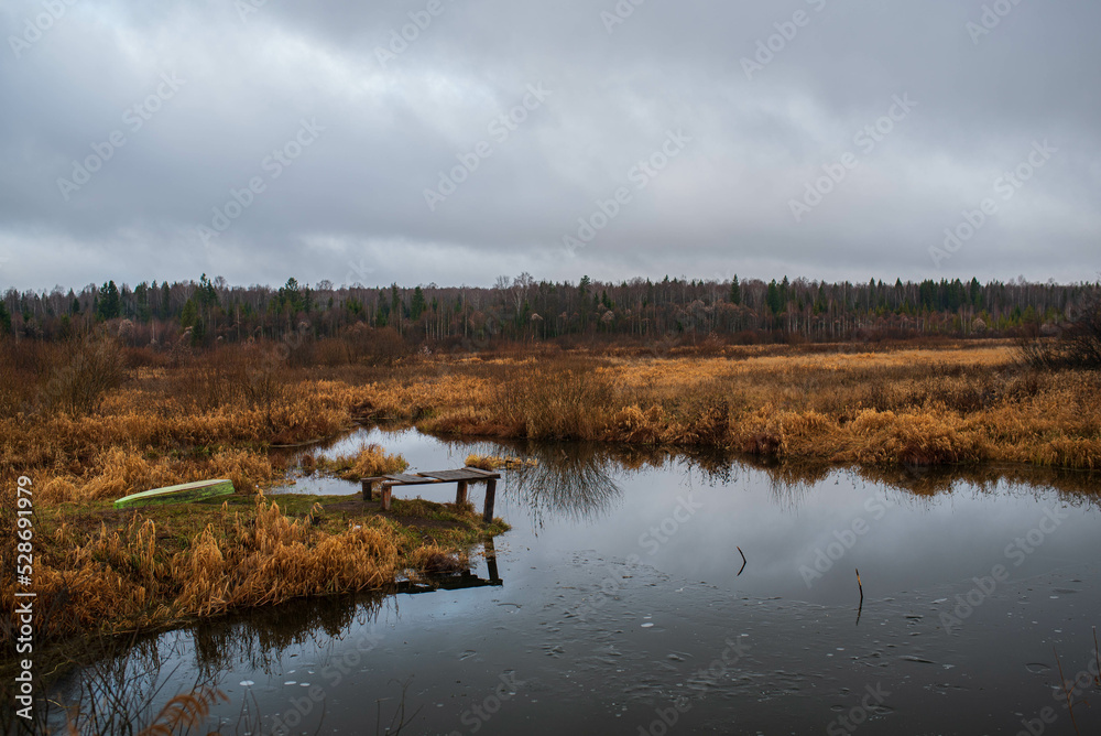 Old rustic wooden jetty on a tranquil lake with wild grasses on the bank and reflections on the water Old rustic wooden jetty on a tranquil lake with wild grasses on the bank and reflections on the water