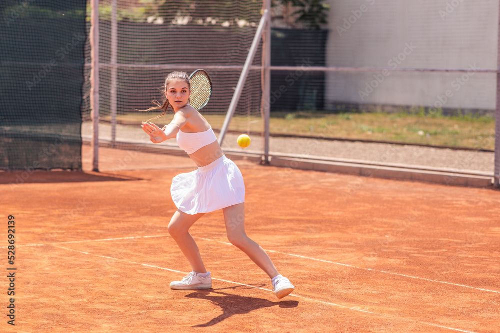 Good looking young woman professional tennis player hitting the ball hard outdoor on the tennis court she wearing uniform concept of healthy lifestyle and professional sport