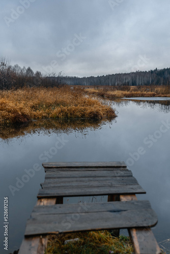 Old rustic wooden jetty on a tranquil lake with wild grasses on the bank and reflections on the water