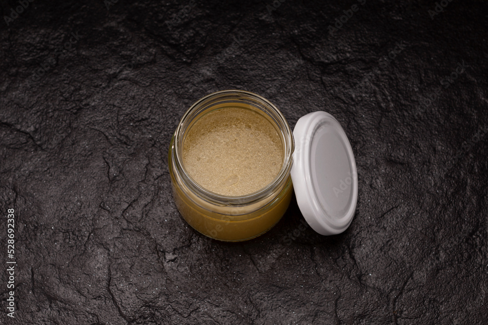 Golden meat bouillon. Beef bone broth in jar on dark stone background
