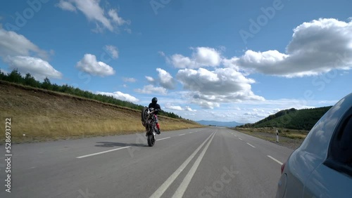 Biker shows off a stunt ride on the back wheel of a motorcycle on the empty mountain road photo
