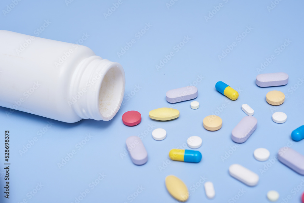 Pile of medical capsules pills in red and white color on blue background, top view for copy space. White medical pills and tablets spilling out of a drug bottle. Macro top down view with copy space.