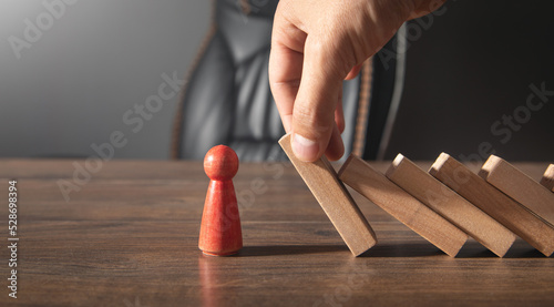 Male hand stopping wooden blocks from falling on human figure.