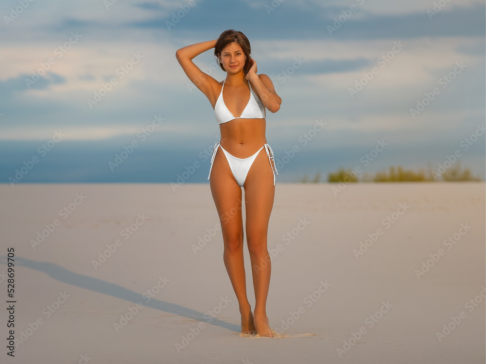 Mockup of a white bikini on a posing girl on the sand, separate clothes with ties on the sides for swimming, for design, advertising.