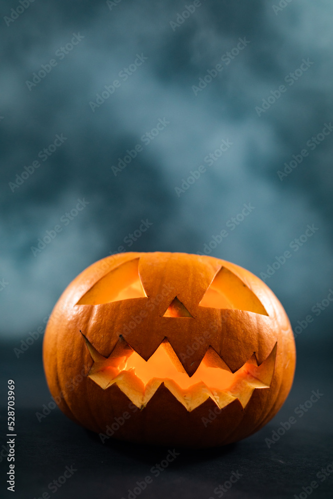 Obraz premium Close up of carved halloween pumpkin against smoke effect on grey background