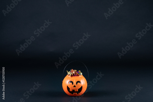 Halloween pumpkin shaped bucket full of candies against black background