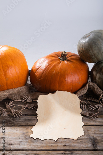 Paper with copy space against pumpkins and skeleton hands on wooden surface against grey background