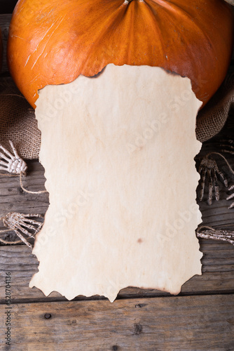 Paper with copy space against pumpkins and skeleton hands on wooden surface against grey background