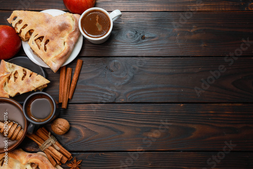 Apple pie slices and black coffee. Bakery food, fresh red apples, cinnamon spice, espresso cups, honey in bowl on dark rustic wooden table background. Traditional autumn dessert flat lay