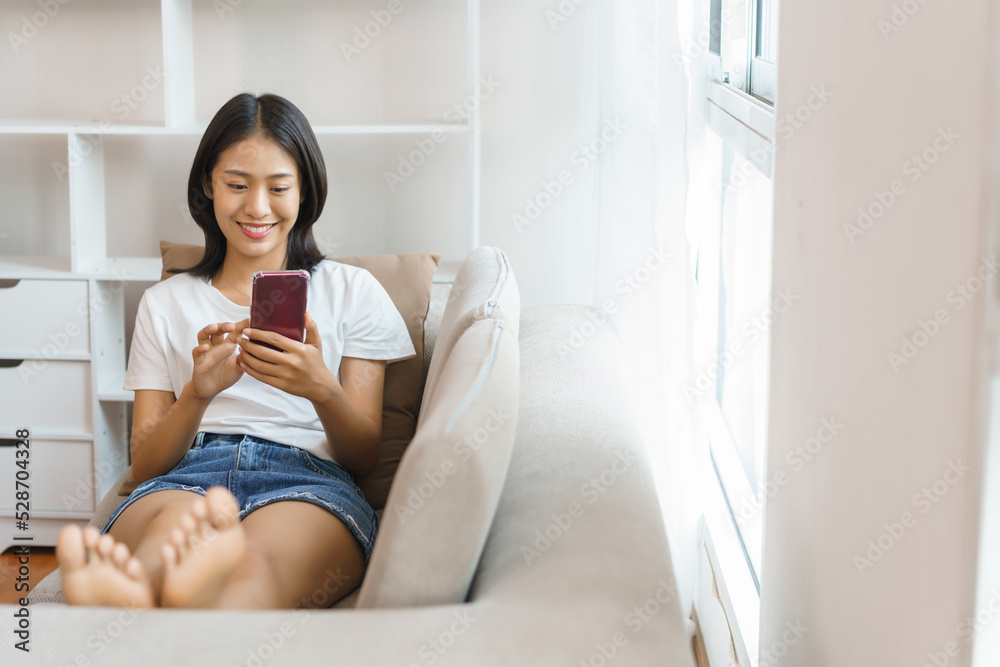 Cozy lifestyle concept, Young woman lying on couch and use smartphone to surf social media at home Cozy lifestyle concept, Young woman lying on couch and use smartphone to surf social media at home