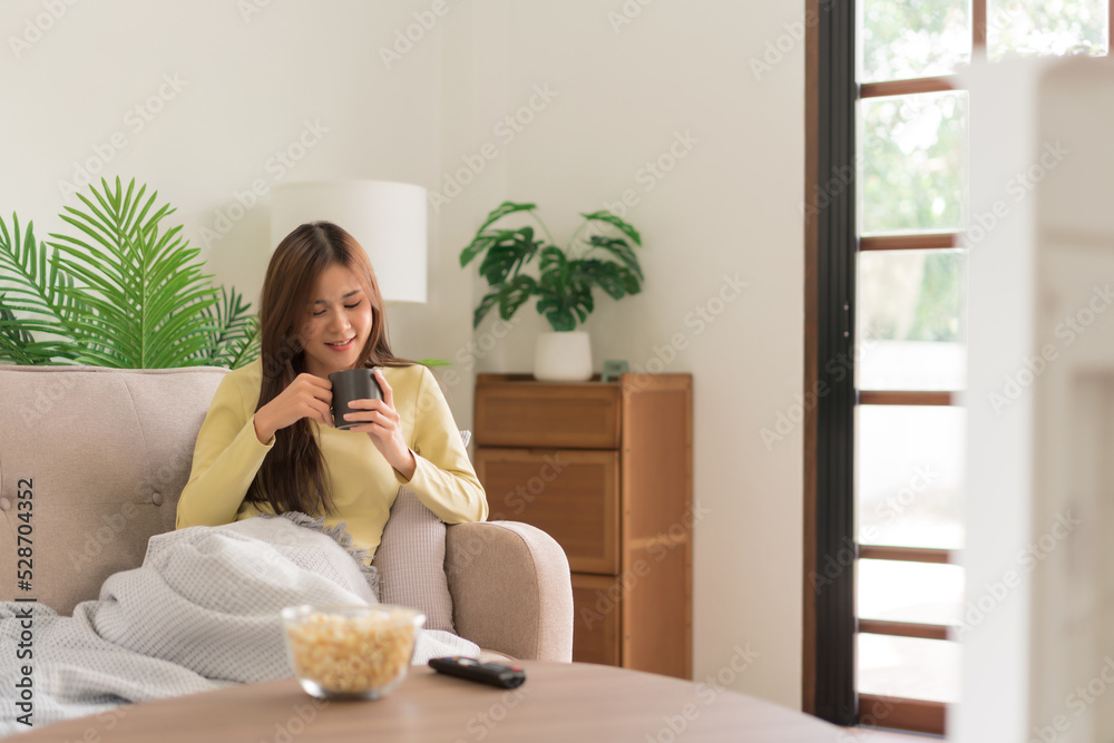 Relaxation concept, Young woman drinking coffee and watching television while lying on the couch Relaxation concept, Young woman drinking coffee and watching television while lying on the couch