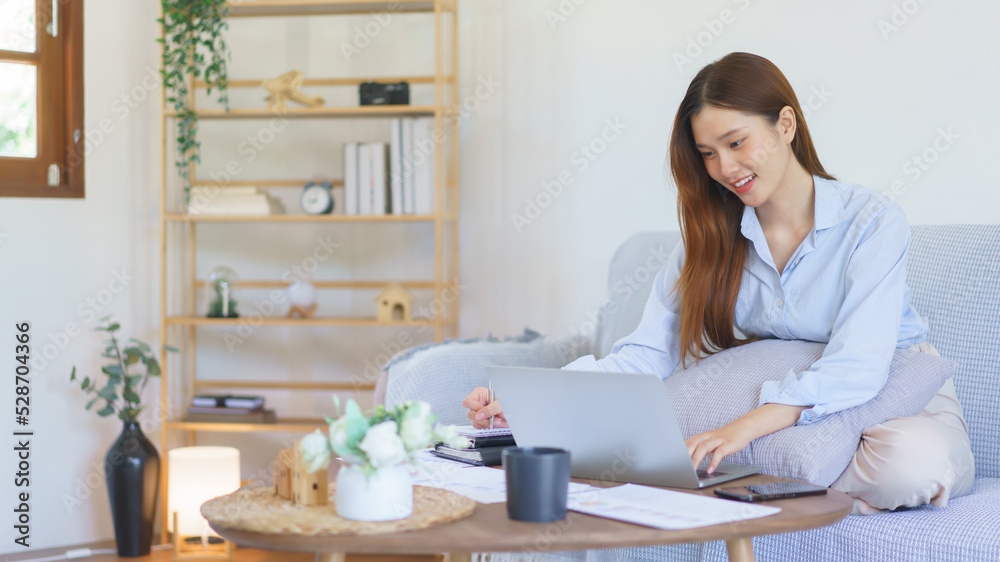 Home office concept, Businesswoman reads marketing plan data on laptop and taking notes on notebook Home office concept, Businesswoman reads marketing plan data on laptop and taking notes on notebook