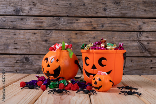 Pumpkin shaped bucket full of halloween candies and toys on wooden surface