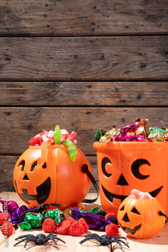 Close up view of pumpkin shaped bucket full of halloween candies and toys on wooden surface