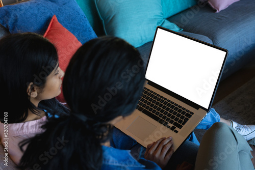 High angle view of biracial mother sitting with daughter using laptop on cough at home