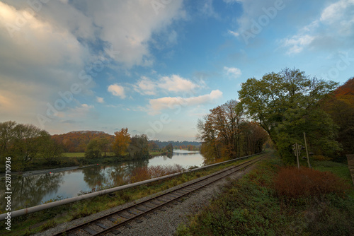 Eisenbahnschienen an einem Fluss mit Wald im Herbst bei blauem Himmel mit Wolken 