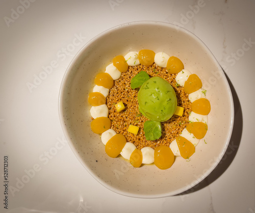 Passion fruit posset dessert with sesame crunch, coconut cream and coriander sorbet on a white dish photo