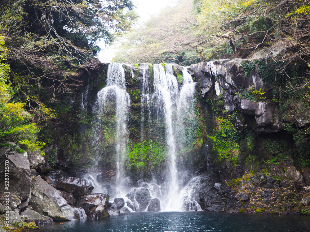 Cheonjeyeon waterfall flanked by rocks and trees in winter, Jeju Island, South Korea