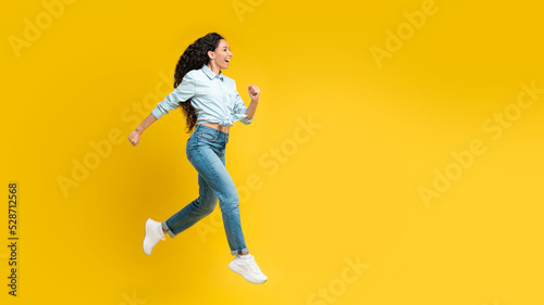 Joyful Arabic Lady Running In Mid Air Over Yellow Background
